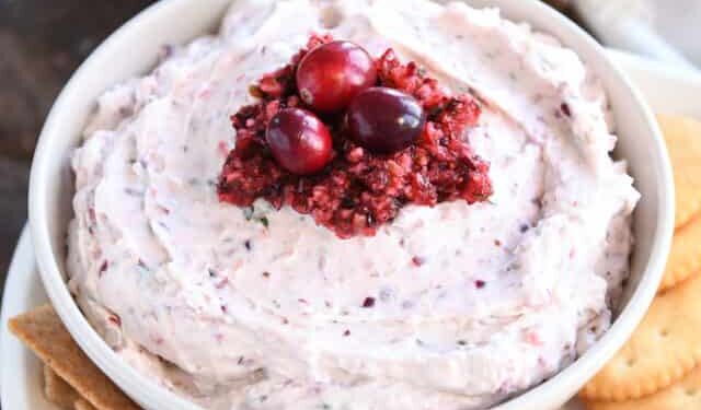 Cream bowl filled with cranberry jalapeno dip and fresh cranberries on top.