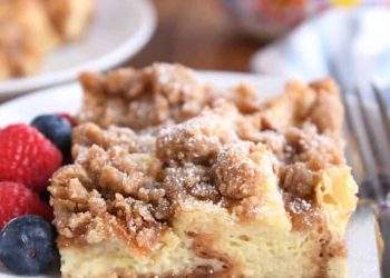 Square serving of French toast bake on white plate with fresh berries and powdered sugar.