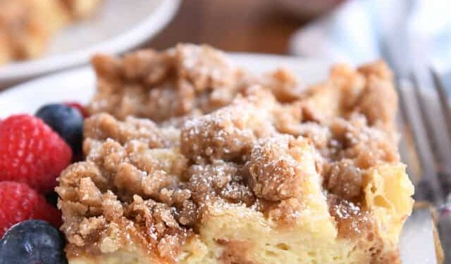 Square serving of French toast bake on white plate with fresh berries and powdered sugar.
