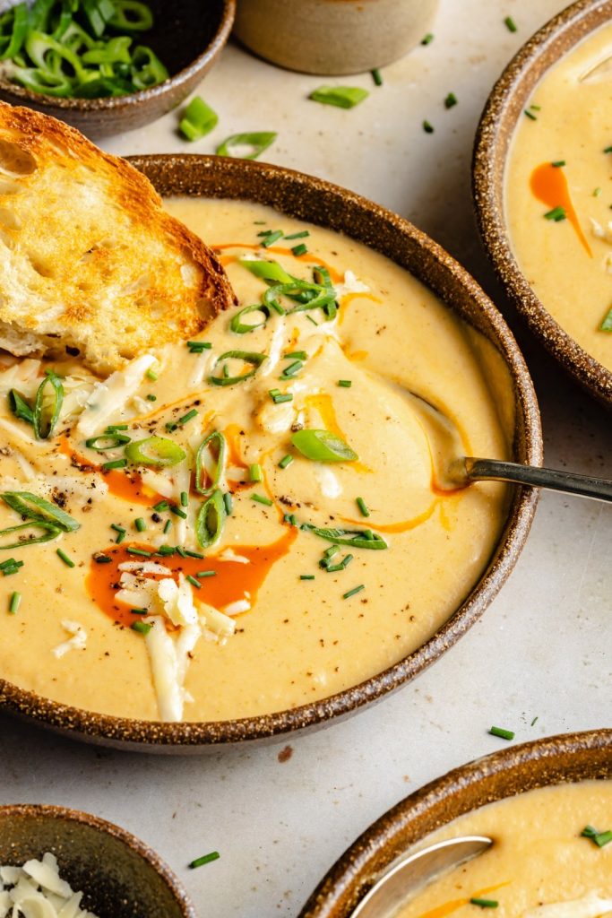 buffalo cauliflower soup in a bowl with a piece of bread