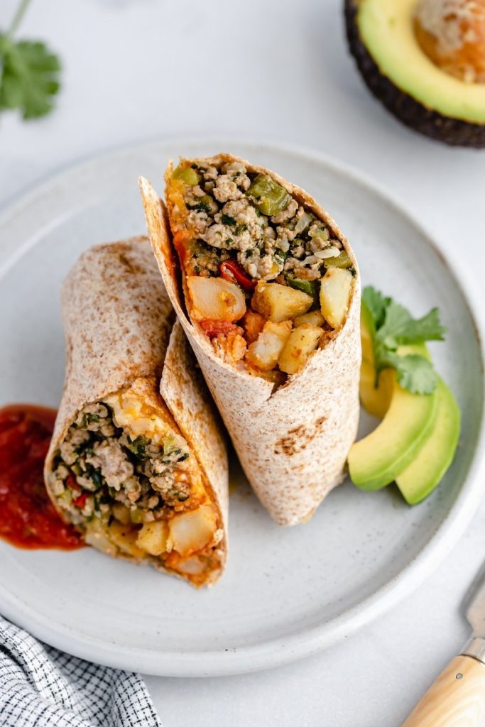 green chile chicken burrito on a plate with avocado and hot sauce