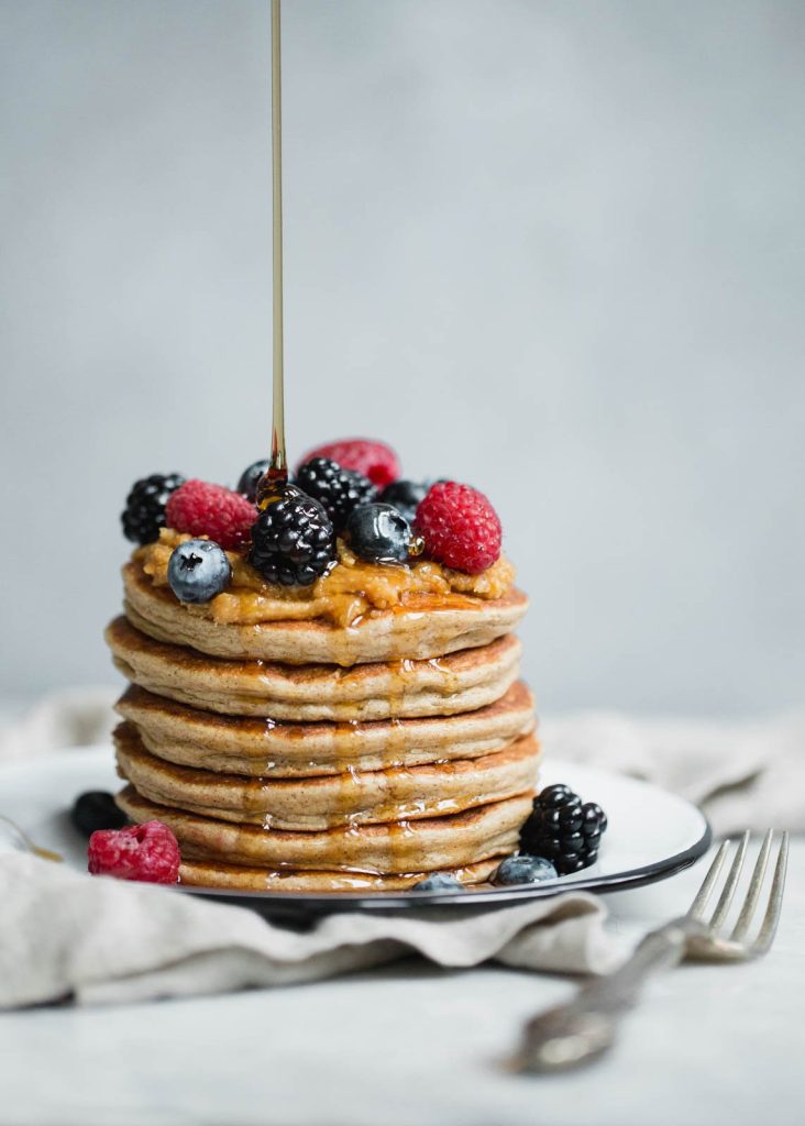 drizzling maple syrup on a stack of cottage cheese pancakes topped with berries