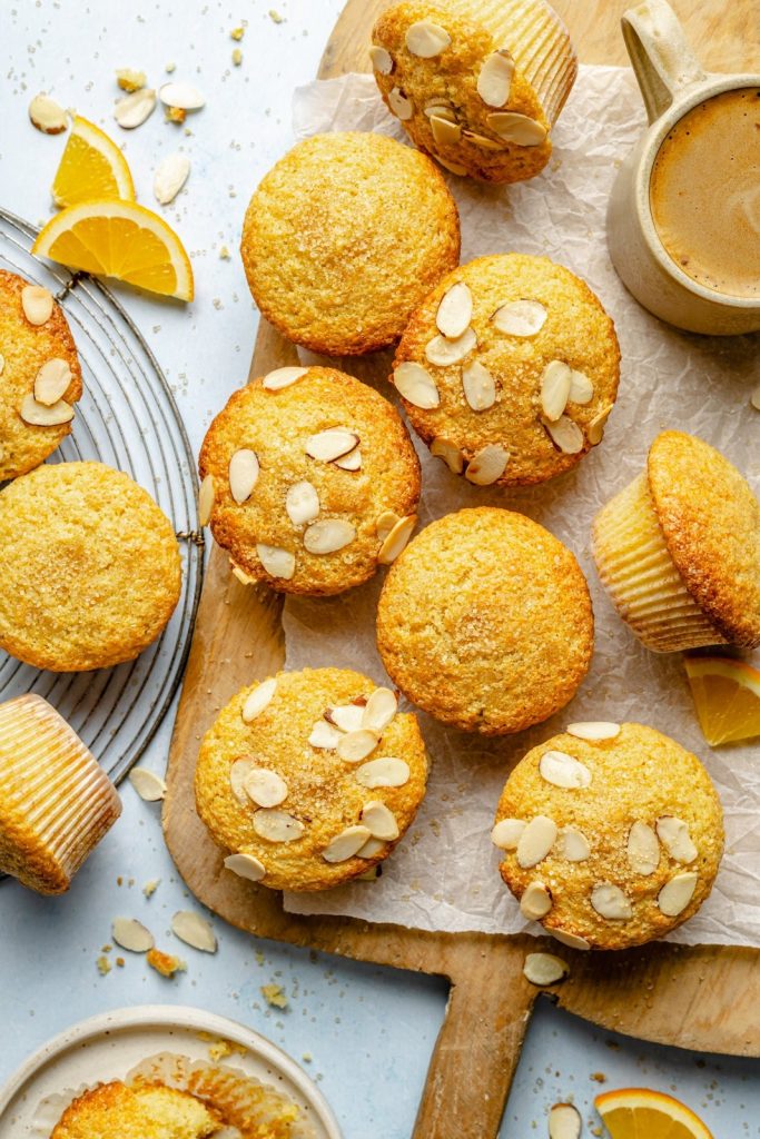 orange muffins topped with sliced almonds on a wooden board