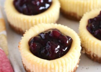 Four mini cheesecakes with huckleberry topping on white tray.