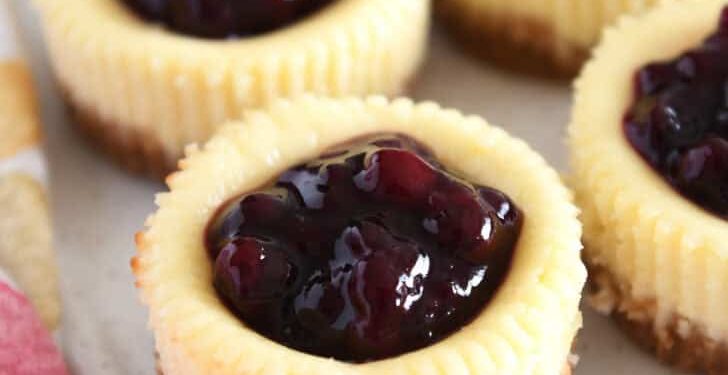 Four mini cheesecakes with huckleberry topping on white tray.