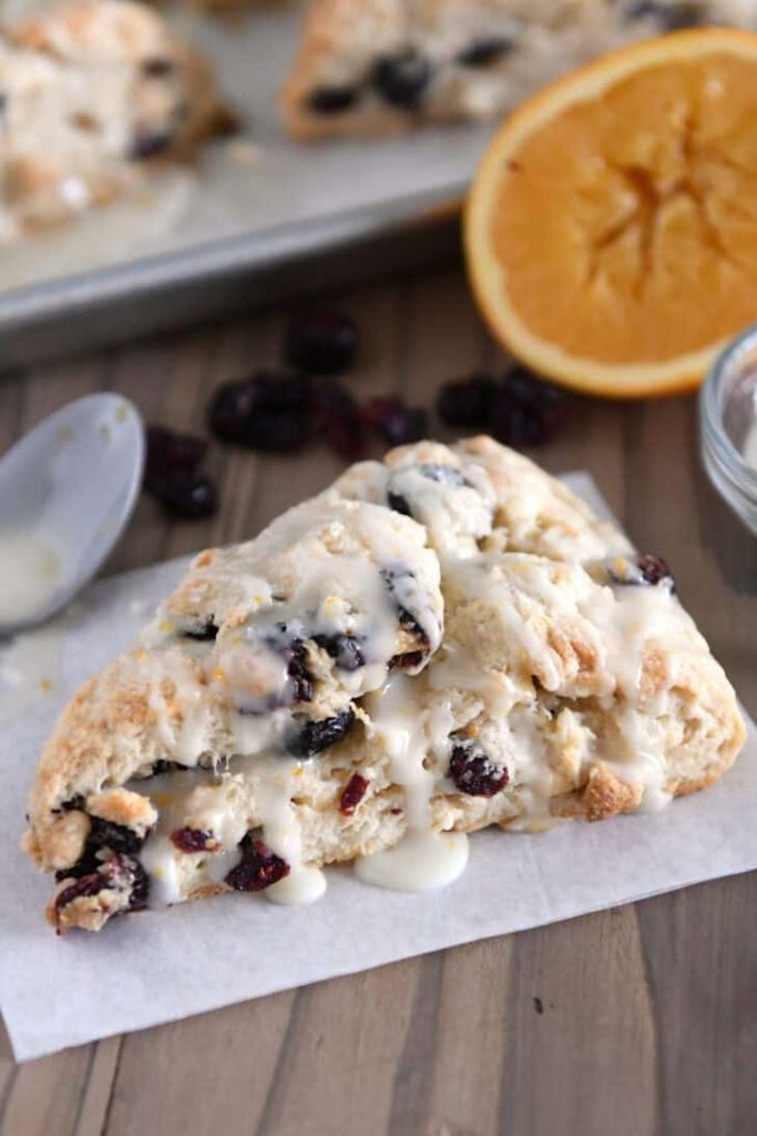 Single cranberry orange scone drizzled with glaze on sheet of parchment paper.