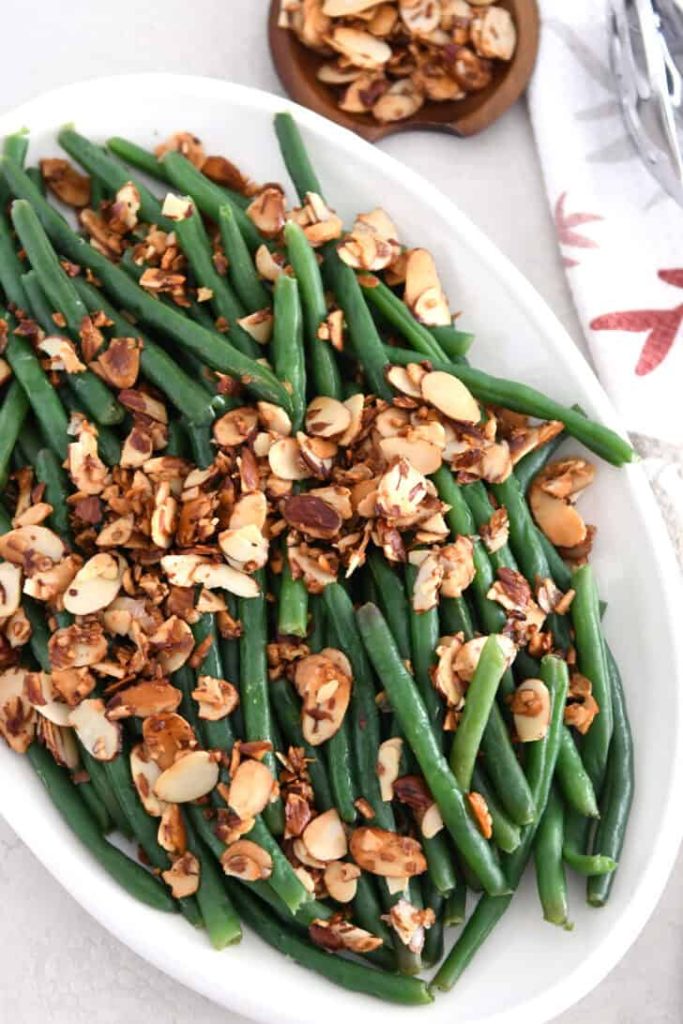 Top down view of sauteed green beans on white tray with toasted almonds.