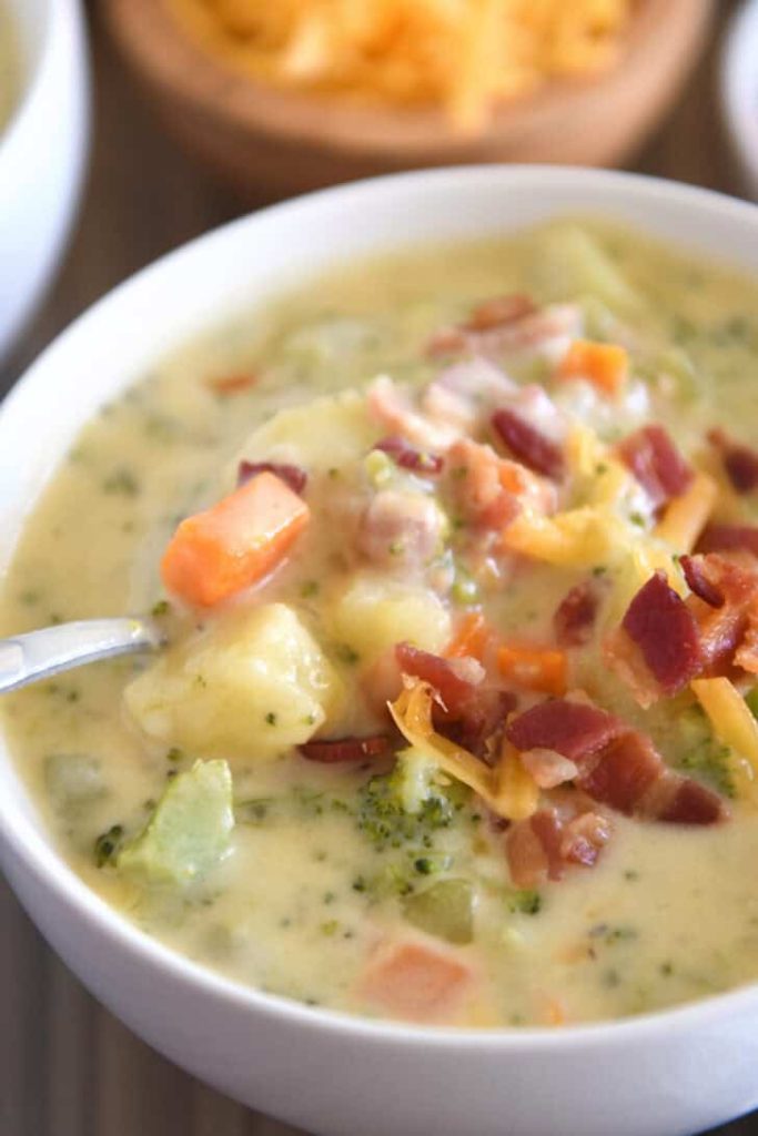 Spoon scooping spoonful of loaded broccoli cheese bacon soup in white bowl.