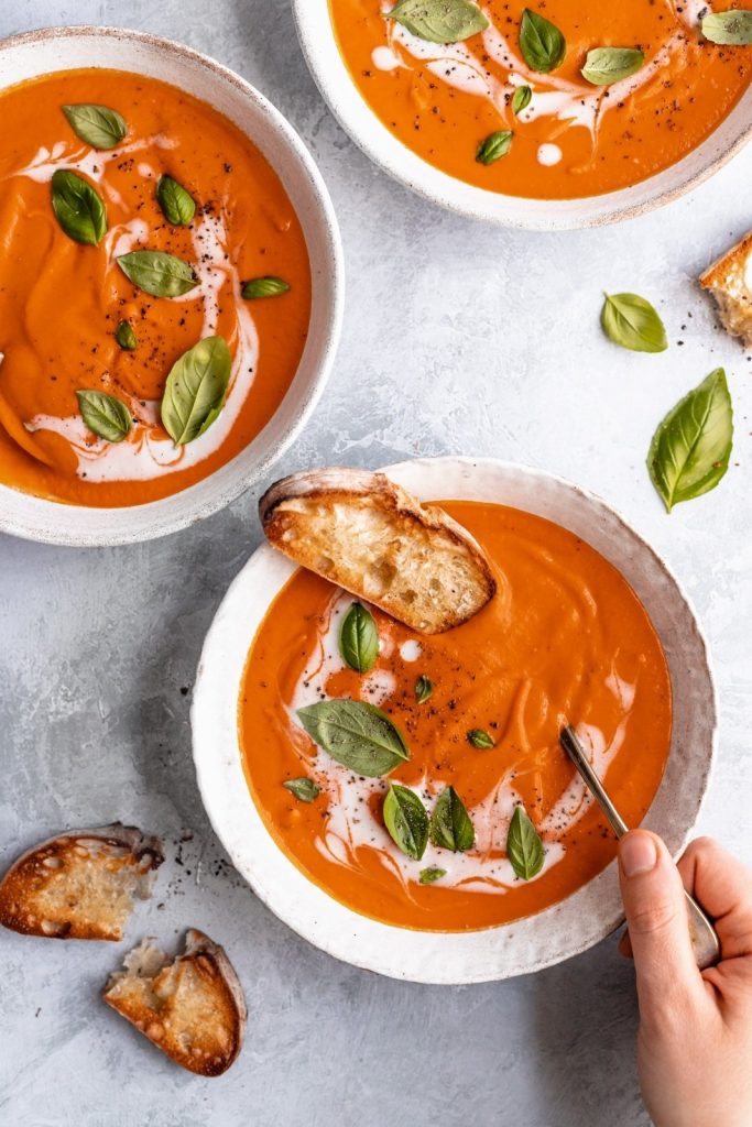 creamy vegan tomato soup in three bowls with garlic bread