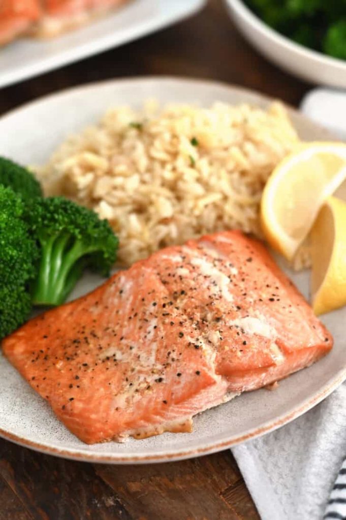 Salmon filet on gray plate with lemon slices, cooked broccoli and rice pilaf.