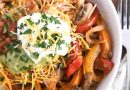 Top down view of white shallow bowl with chicken, vegetables, cheese, sour cream and guacamole.