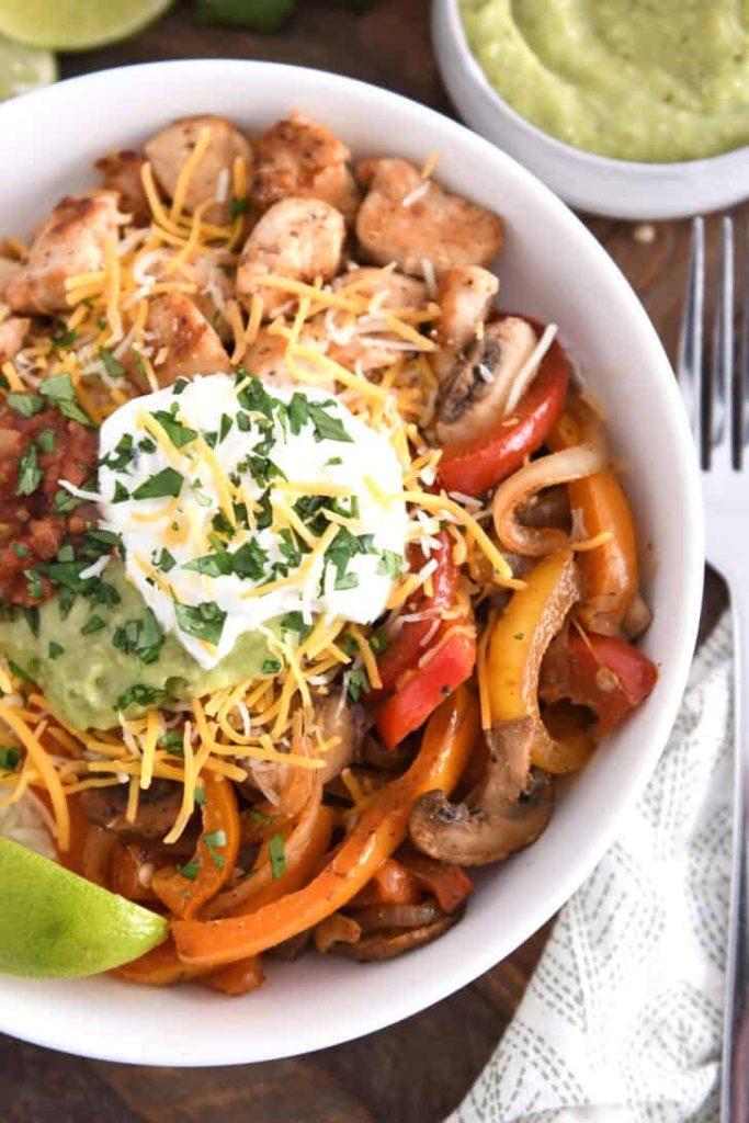 Top down view of white shallow bowl with chicken, vegetables, cheese, sour cream and guacamole.