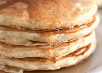 Stack of four pancakes on white plates with syrup drizzled down the side.