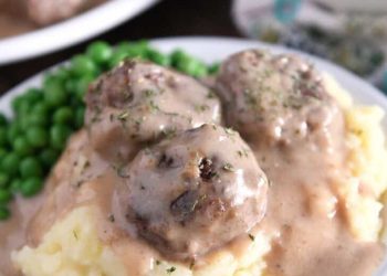 Three meatballs on top of pile of mashed potatoes smothered in thick brown gravy.