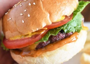 Pressing juicy burger topped with cheese, lettuce, tomato and mustard on homemade bun.